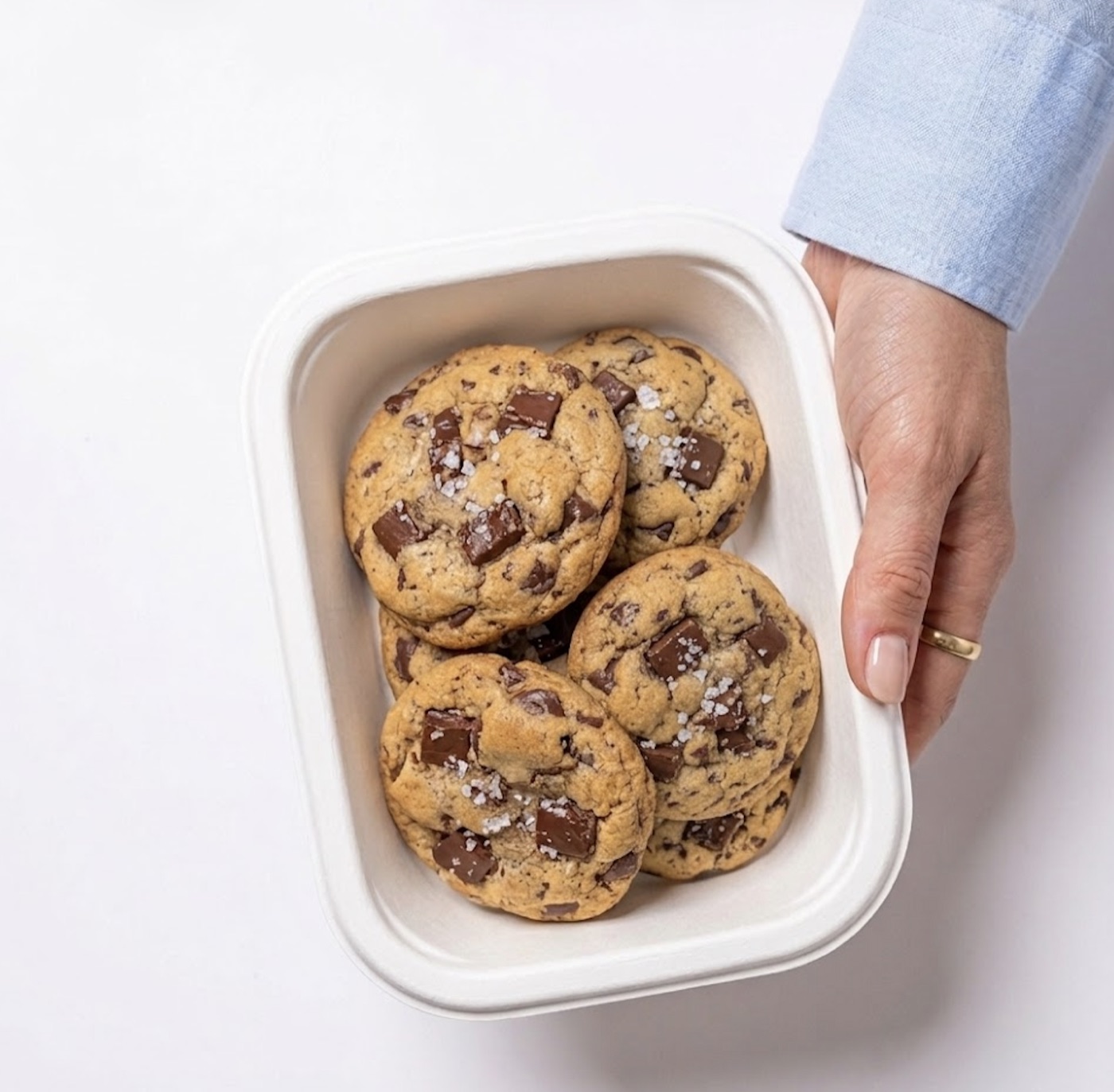 a hand holding a tray of fresh chocolate-chunk protein cookies with flaky salt