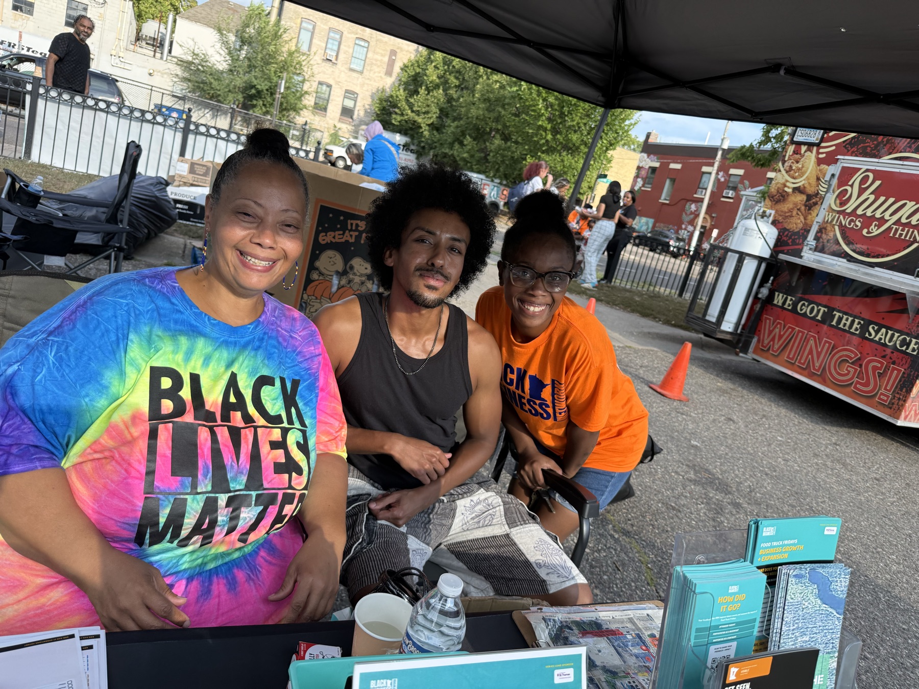 omar at a community event table in minneapolis, sitting with two neighborhood volunteers