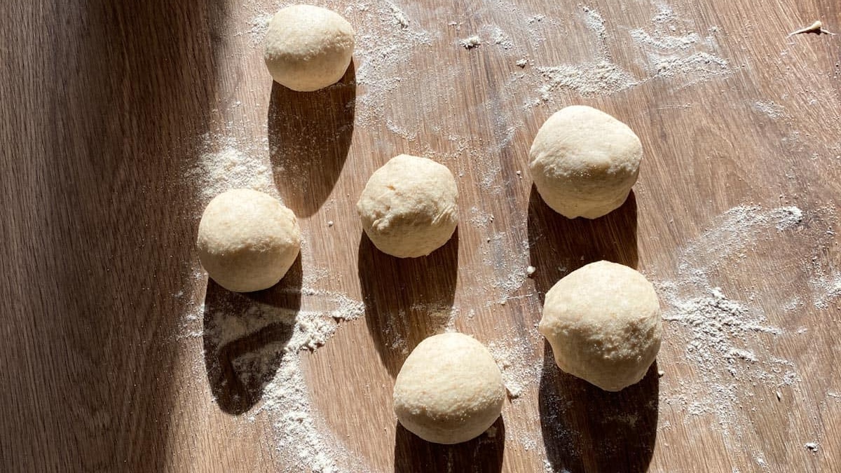 six hand-rolled dough balls resting on a floured wooden table in the tandoco kitchen